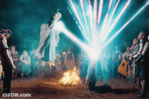 A Group Of People Are Standing Around A Fire With A Blue Light Coming Out Of The Sky GIF