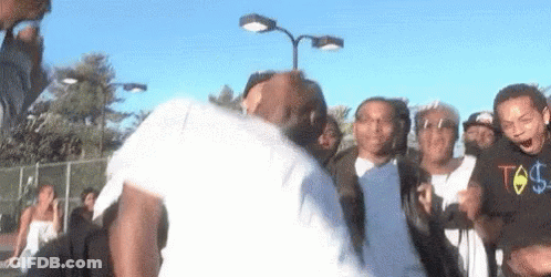 A Group Of People Are Standing Around A Man In A White Shirt With A Dollar Sign On The Front . GIF
