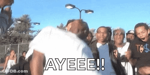 A Group Of People Are Standing Around A Man In A White Shirt With The Word Ayeeee Written On It . GIF