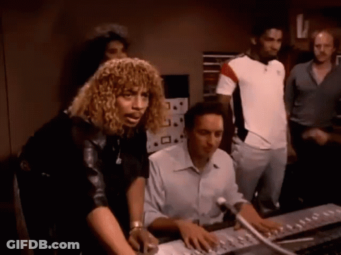A Group Of People Are Standing Around A Man Sitting At A Desk GIF