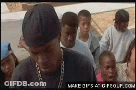 A Group Of People Are Standing Around A Man Wearing A Chain Around His Neck GIF