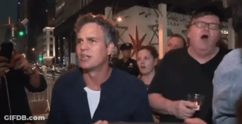 A Group Of People Are Standing Around A Man Who Is Holding A Glass Of Beer . GIF