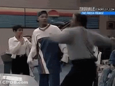 A Group Of People Are Standing Around A Table And A Man Is Standing In The Middle Of The Room . GIF