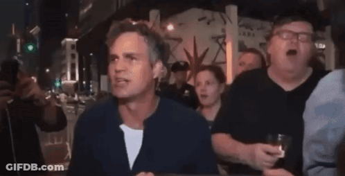 A Group Of People Are Standing Around A Table And One Of Them Is Holding A Glass Of Whiskey GIF