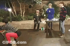 A Group Of People Are Standing Around A Table In A Room With Trees In The Background . GIF