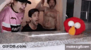 A Group Of People Are Standing Around A Table With A Stuffed Elmo . GIF