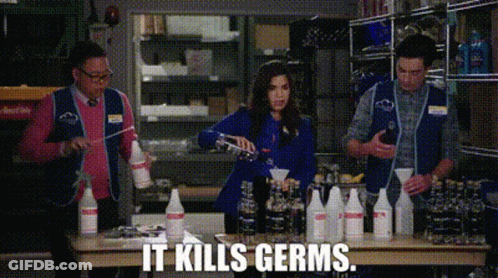 A Group Of People Are Standing Around A Table With Bottles Of Cleaning Supplies And The Words `` It Kills Germs '' . GIF