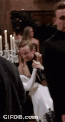 A Group Of People Are Standing Around A Table With Candles And A Man Holding A Microphone . GIF