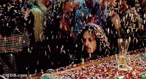 A Group Of People Are Standing Around A Table With Confetti Falling On Them . GIF