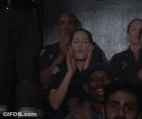 A Group Of People Are Standing In A Dark Room And One Of Them Is Wearing A Black Shirt With The Letter T On It GIF