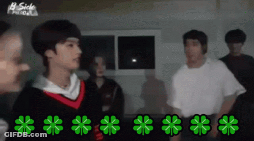 A Group Of People Are Standing In A Dark Room With Green Clovers On The Floor GIF