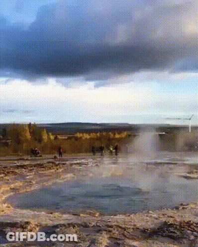 A Group Of People Are Standing In A Field Near A Waterfall GIF