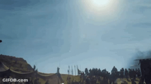 A Group Of People Are Standing In A Field With A Tent In The Background . GIF
