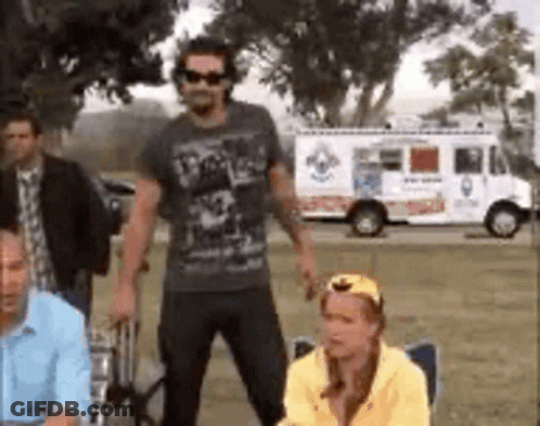 A Group Of People Are Standing In A Field With A White Truck In The Background . GIF
