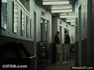 A Group Of People Are Standing In A Hallway Talking To Each Other . GIF