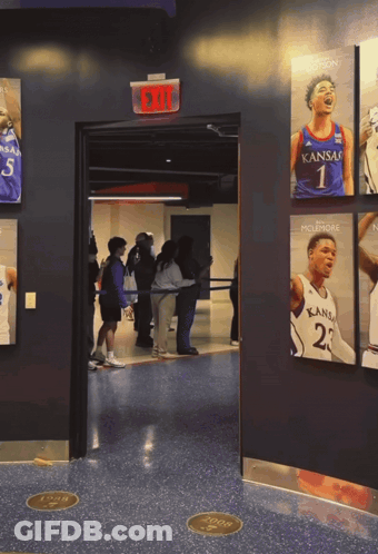 A Group Of People Are Standing In A Hallway With A Kansas Basketball Player On The Wall GIF