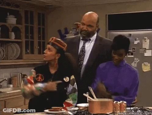 A Group Of People Are Standing In A Kitchen And One Of Them Has Her Fist Up GIF
