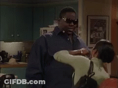 A Group Of People Are Standing In A Living Room Talking To Each Other . GIF