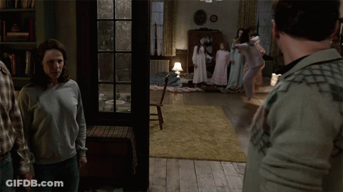 A Group Of People Are Standing In A Living Room With A Book Titled " The Conjuring " In The Background GIF