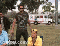 A Group Of People Are Standing In A Park In Front Of A Pizza Truck GIF