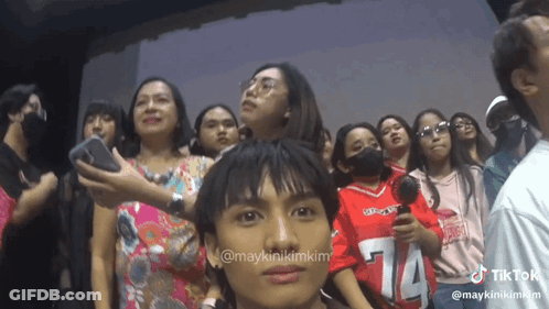 A Group Of People Are Standing In A Room And One Of Them Is Wearing A Red Shirt With The Number 14 On It GIF