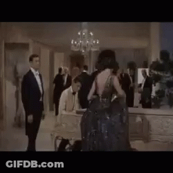 A Group Of People Are Standing In A Room With A Chandelier . GIF