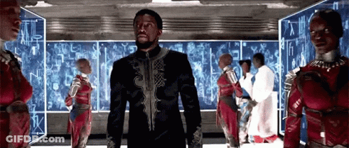 A Group Of People Are Standing In A Room With A Man In A Black Suit Standing In The Middle . GIF