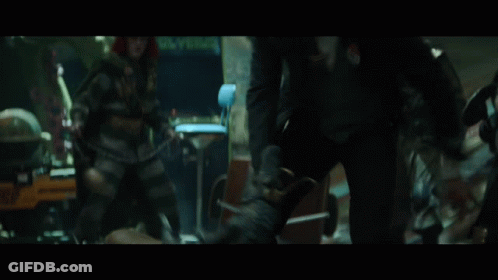 A Group Of People Are Standing In A Room With A Man Wearing A Green Suit GIF