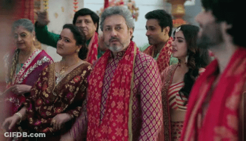 A Group Of People Are Standing In A Room With A Man Wearing A Red Scarf Around His Neck . GIF