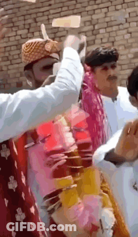 A Group Of People Are Standing In Front Of A Brick Wall And One Of Them Is Wearing A Turban GIF