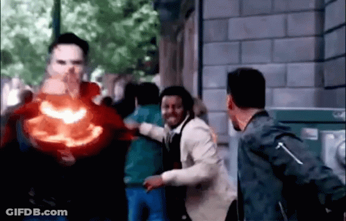 A Group Of People Are Standing In Front Of A Building While A Man Is Holding A Red Object In His Hand . GIF