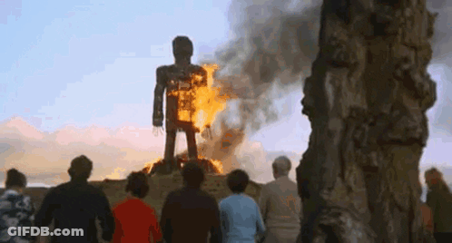 A Group Of People Are Standing In Front Of A Burning Statue Of A Man . GIF
