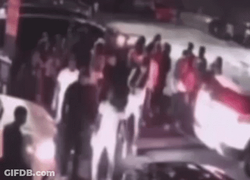 A Group Of People Are Standing In Front Of A Car With A Fire Coming Out Of It . GIF