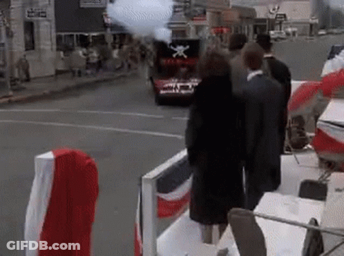 A Group Of People Are Standing In Front Of A Car With A Flag On The Back . GIF