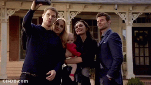 A Group Of People Are Standing In Front Of A House Taking A Selfie With A Baby . GIF