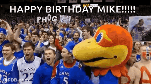 A Group Of People Are Standing In Front Of A Mascot And A Sign That Says `` Happy Birthday Mike '' . GIF