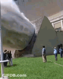 A Group Of People Are Standing In Front Of A Pyramid In A Park . GIF