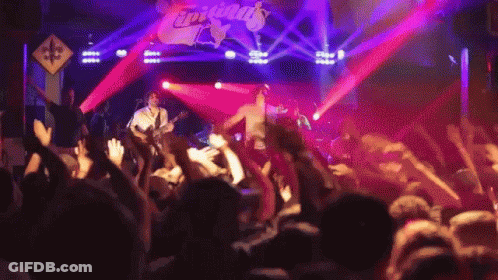 A Group Of People Are Standing In Front Of A Stage That Has The Word Tropicals On It GIF