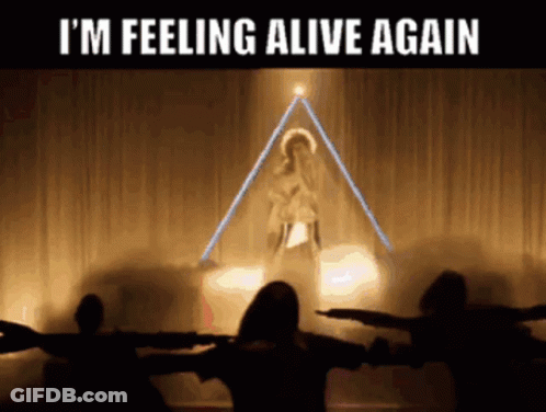 A Group Of People Are Standing In Front Of A Stage With The Words I 'M Feeling Alive Again GIF