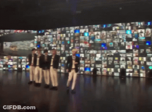 A Group Of People Are Standing In Front Of A Wall Of Pictures GIF
