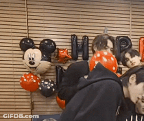 A Group Of People Are Standing In Front Of A Wall With Mickey Mouse Balloons And Letters . GIF