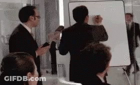 A Group Of People Are Standing In Front Of A White Board . GIF