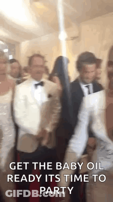 A Group Of People Are Standing Next To Each Other In A Room And One Of Them Is Holding A Baby Oil Bottle . GIF