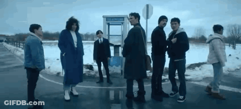 A Group Of People Are Standing Next To Each Other On The Side Of The Road In Front Of A Pay Phone Booth . GIF