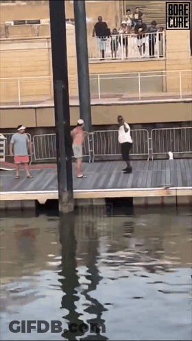 A Group Of People Are Standing On A Dock With A Sign That Says Bore The Cure On It GIF