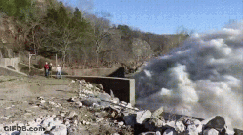A Group Of People Are Standing On A Rocky Shoreline Looking At A Waterfall . GIF