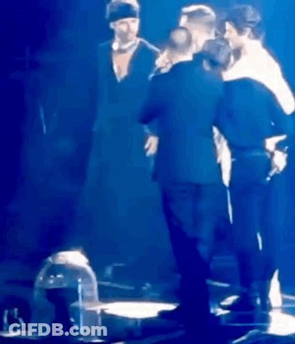 A Group Of People Are Standing On A Stage In Front Of A Microphone . GIF