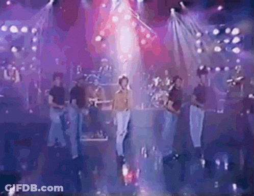 A Group Of People Are Standing On A Stage In Front Of A Stage With Purple Lights . GIF