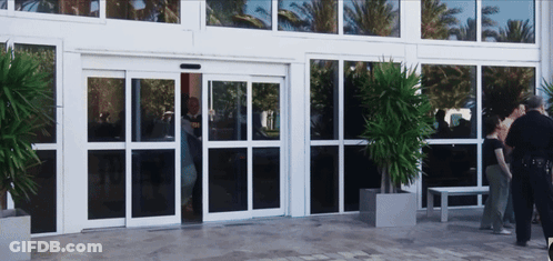 A Group Of People Are Standing Outside Of A Building With A Sliding Glass Door GIF