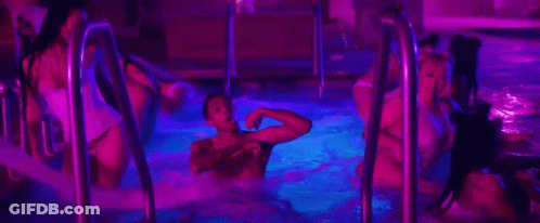 A Group Of People Are Swimming In A Swimming Pool At Night . GIF